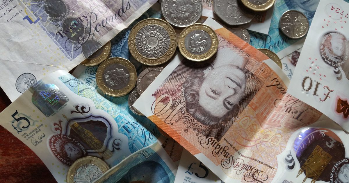 A scattered pile of British banknotes and coins, including five, ten and twenty pound notes and one and two pound coins.