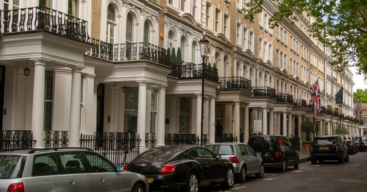 A row of grand white-stuccoed period townhouses on a London street, with cars parked outside and an estate agent's letting board.