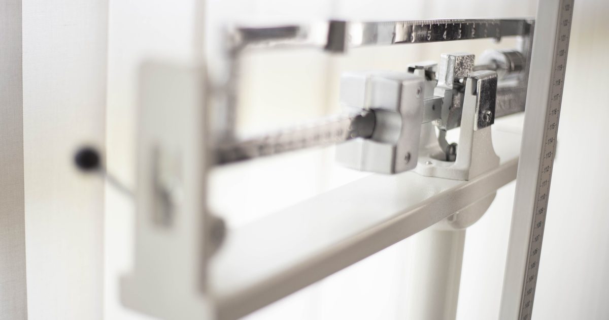 Close-up of a mechanical balance-beam weighing scale, with sliding weights on a numbered metal beam.